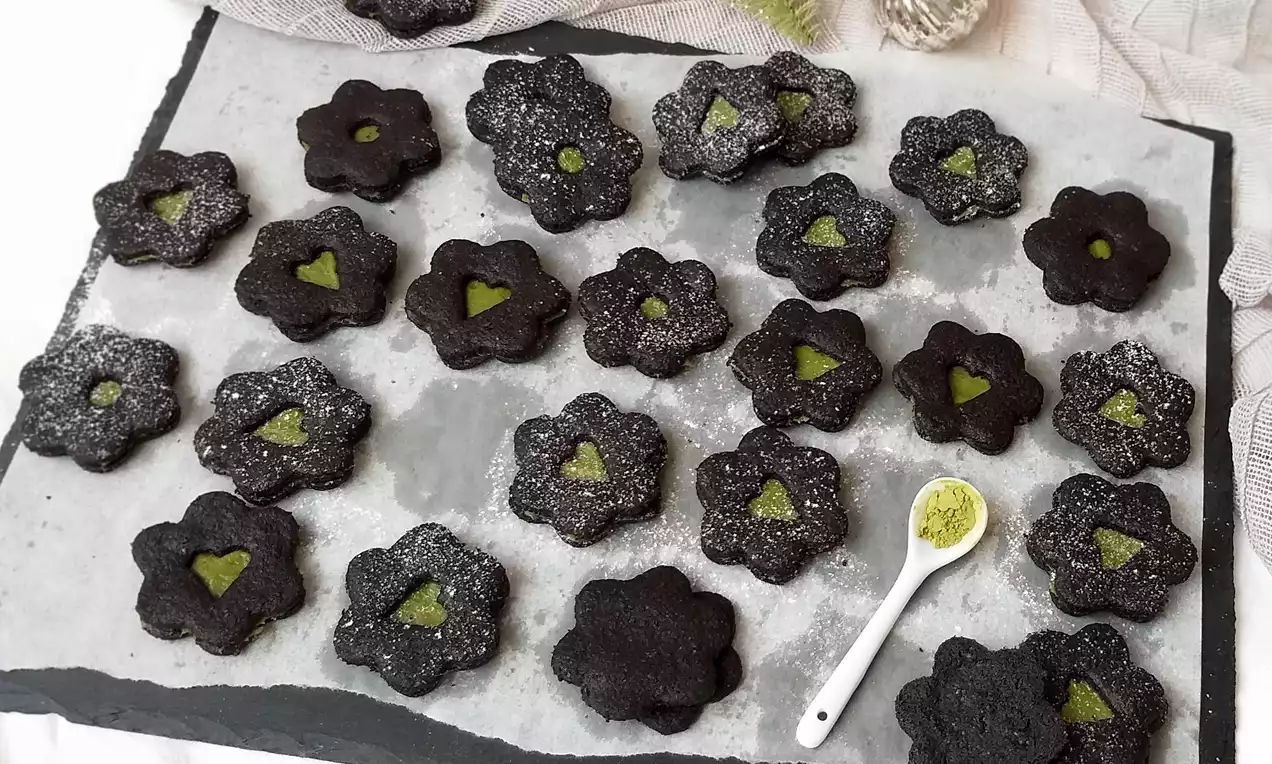 Celozrnné kakaové kvetinky s matcha ganache uprostred, posypané jemným práškovým cukrom, rozložené na šedom bridlicovom podnose