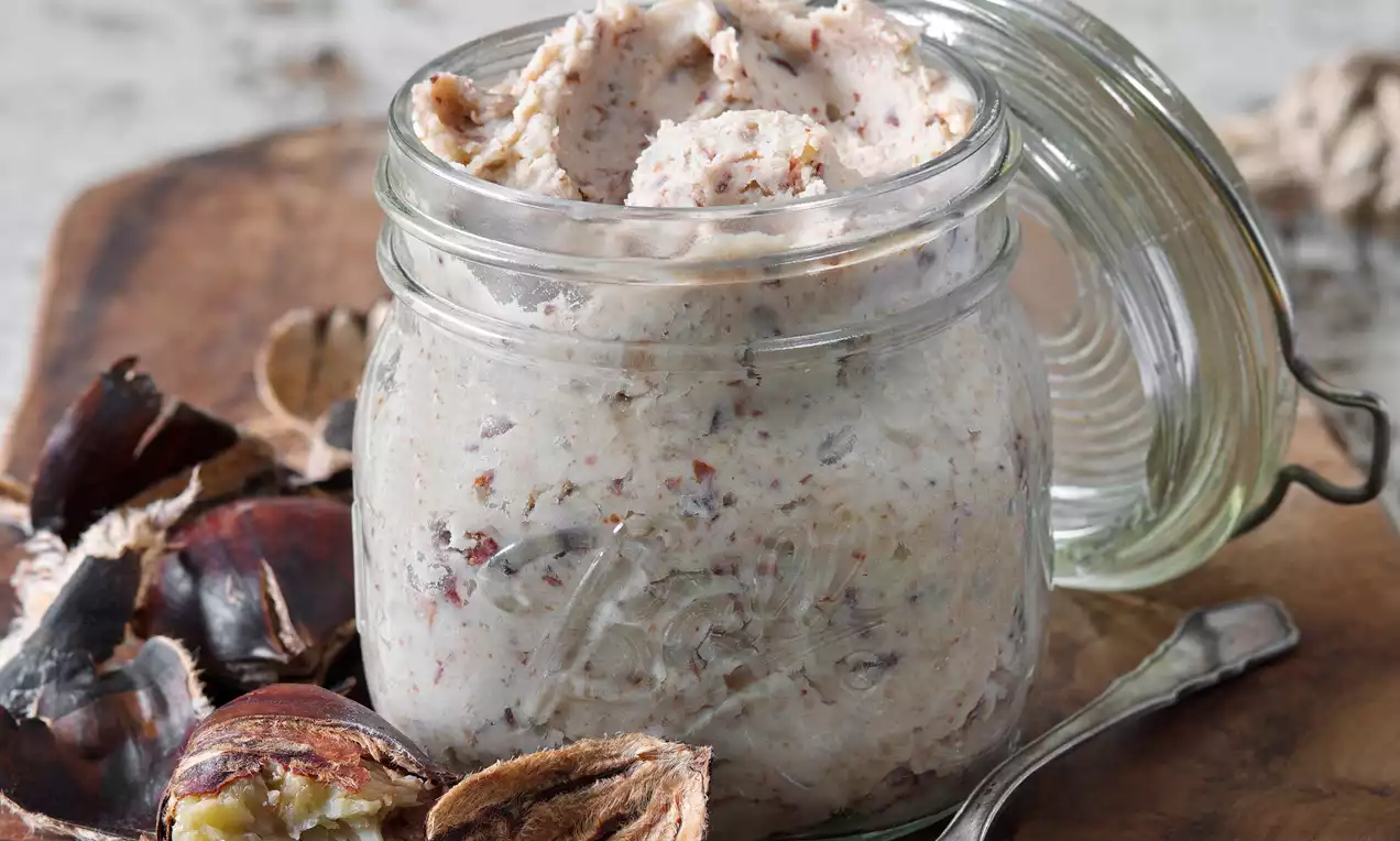 Husté kaštanové pyré s jemnou zrnitou štruktúrou v priehľadnom zaváraninovom pohári, vedľa rozlúsknutých gaštanov a kovovej lyžičky