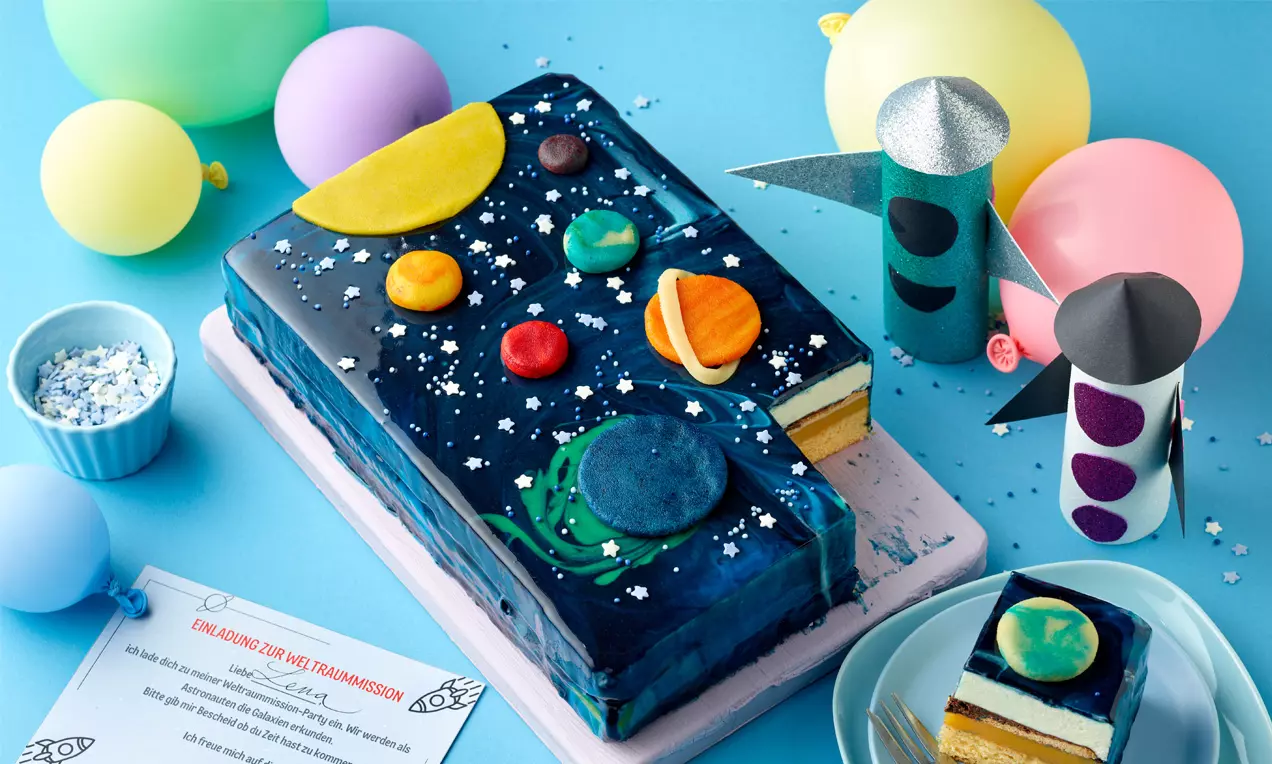 Rechteckiger Kuchen mit glänzender blauer Glasur, bunten Planeten aus Fondant und weißen Sternen auf einer hellblauen Platte drapiert