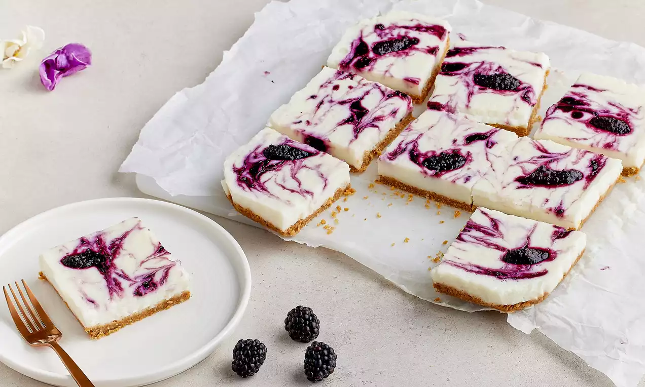 Kıtır bisküvi tabanlı kare dilimli tatlı, kremsi beyaz puding katmanı üzerine mor böğürtlen sosu ve bütün böğürtlenlerle süslenmiş
