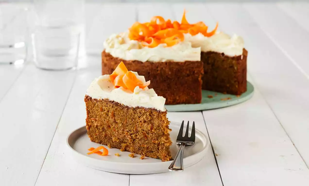 Kosteapintainen, lämpimänruskea porkkanakakku valkoisella kuorrutteella, koristeena appelsiininvärisiä porkkanakiehkuroiden spiraaleja