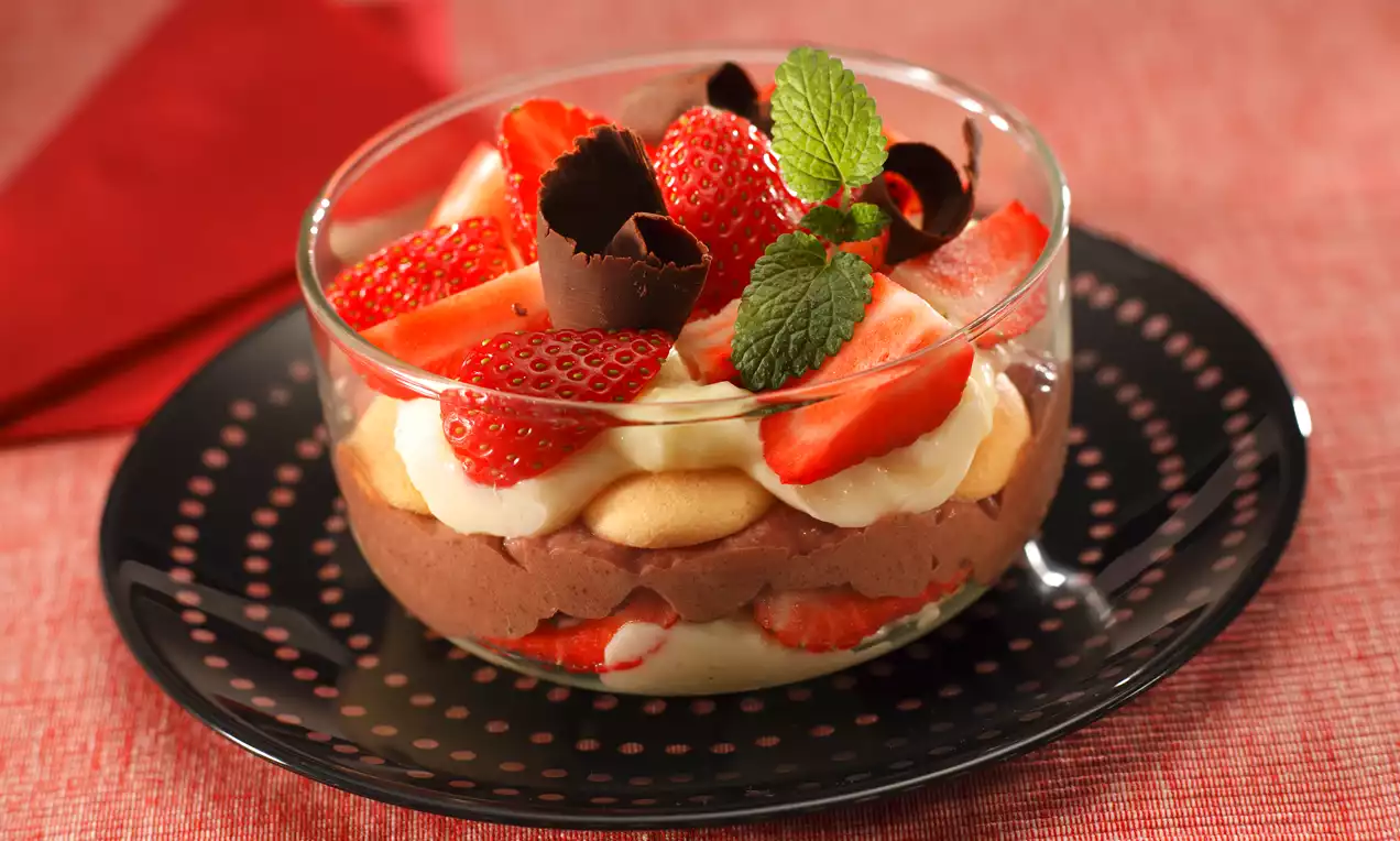 Trasený pohár s vrstvami krémovej čokoládovej a vanilkovej náplne, piškót, čerstvých jahôd, čokoládových dekorácií a lístkov mäty