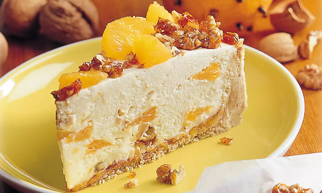 Walnuss-Orangentorte mit heller Füllung, eingebetteten Fruchtstücken, knusprigem Boden und karamellisierten Walnüssen auf gelbem Teller