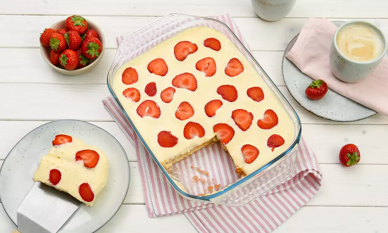 Erdbeer-Tiramisu u staklenom pravokutnom kalupu s kremastim slojem svijetložute boje posutim kriškama svježih jagoda na bijelom stolu
