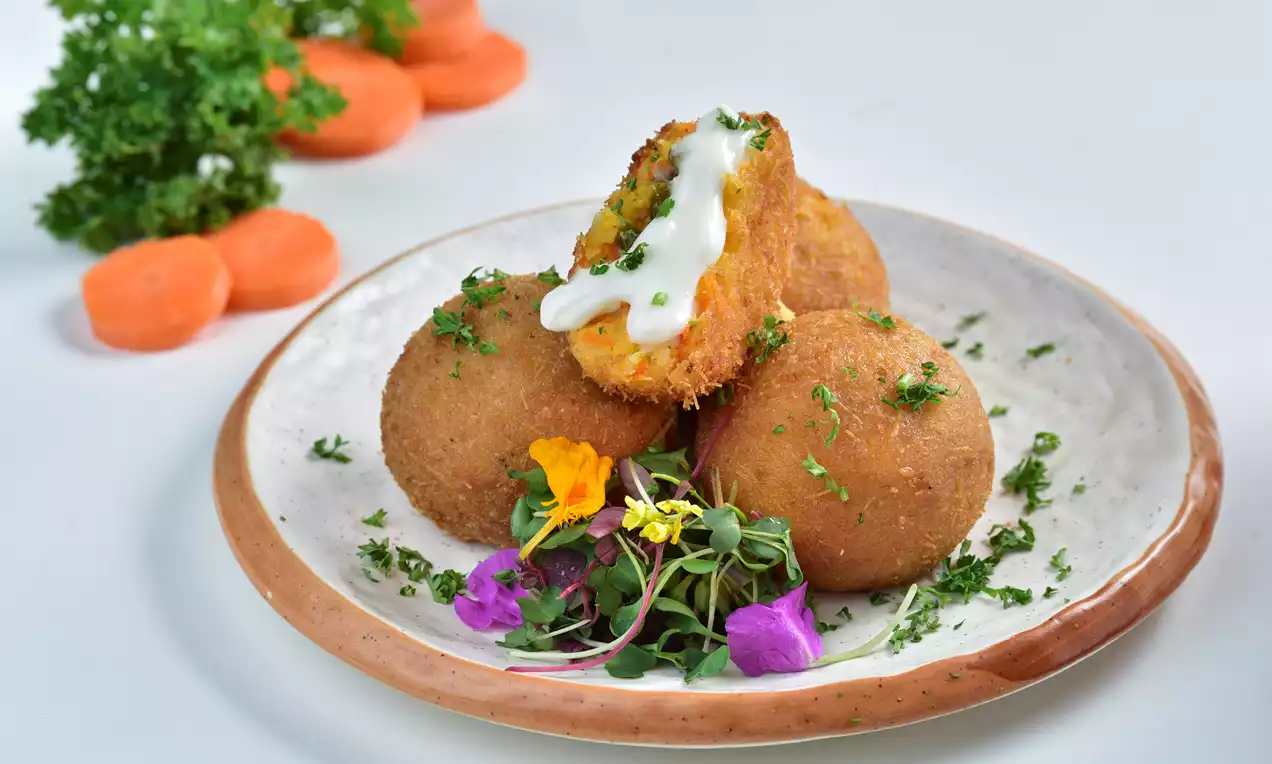 Golden-brown crispy rice balls on a white plate with fresh herbs, vibrant edible flowers, and a dollop of creamy mayo drizzling over