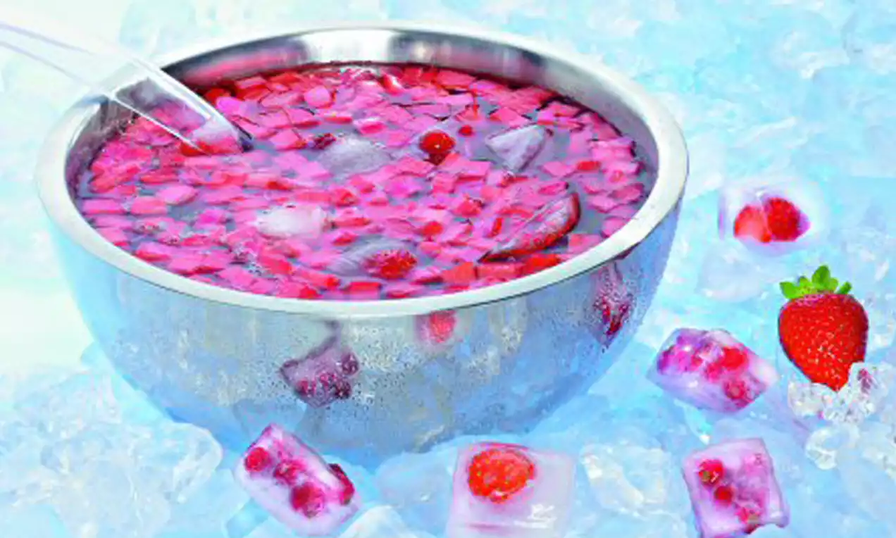 Rote Rhabarber-Bowle mit Beerenstücken und transparenten Eiswürfeln, serviert in einer silbernen Schale auf zerstoßenem Eis mit Erdbeerdekoration