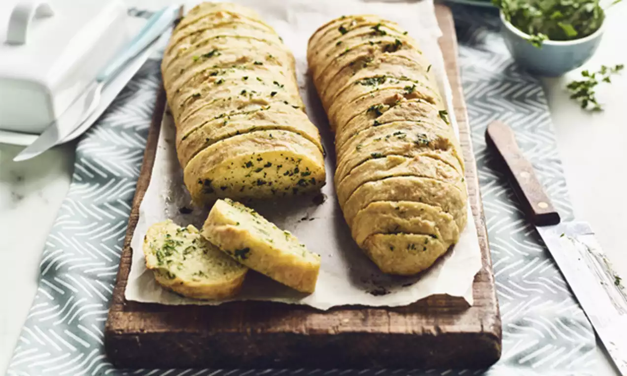 Golden garlic bread sliced into even pieces, speckled with green herbs, arranged on parchment paper over a wooden board