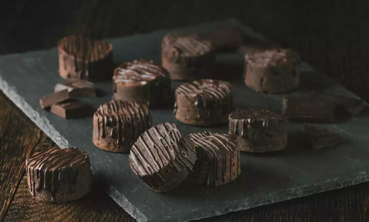 Rondele mici și compacte din ciocolată neagră lucioasă cu dungi fine decorativ turnate, aranjate pe o placă de ardezie gri-închis