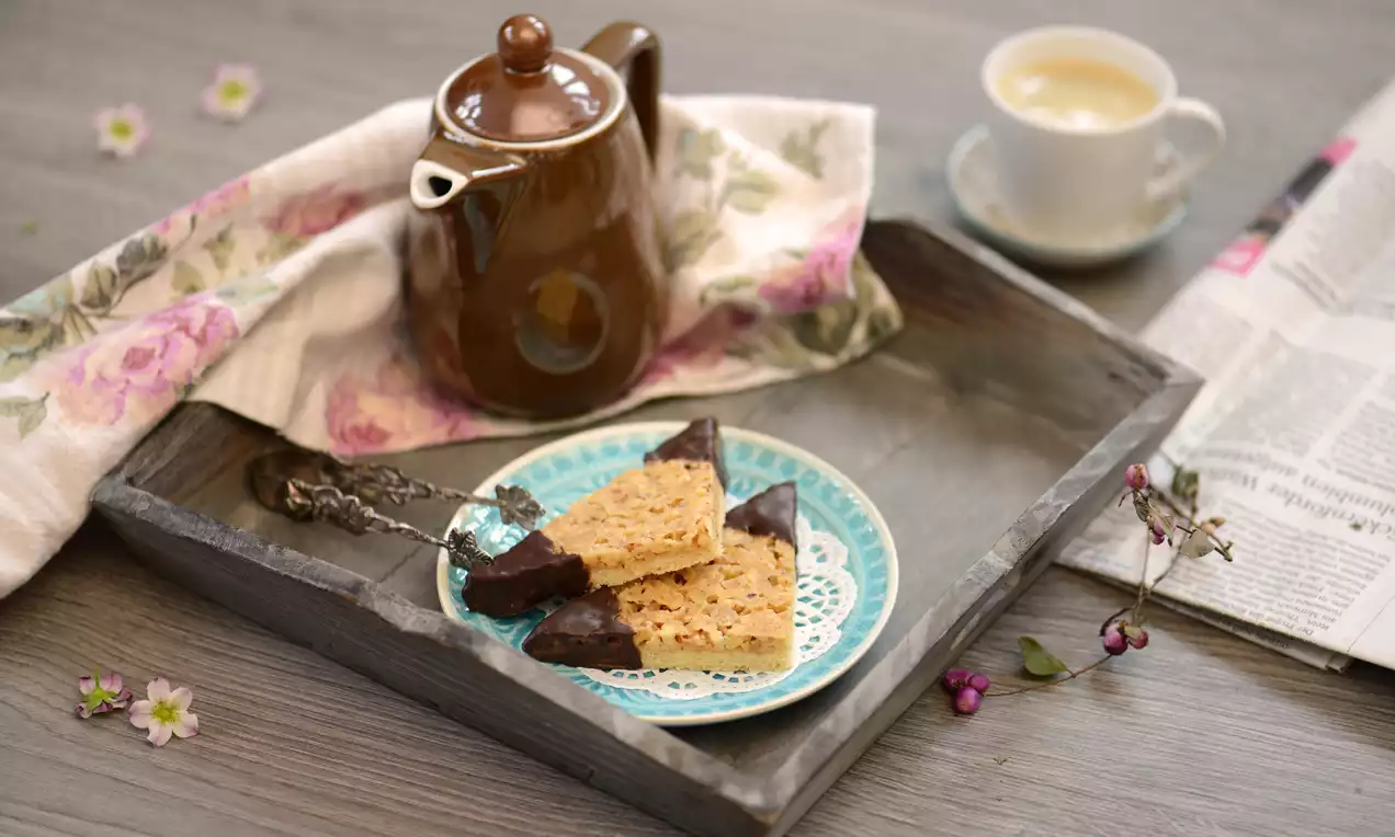 Dreieckige Nussecken mit goldbrauner Oberfläche und dunkler Schokoladenecke auf einem blau gemusterten Teller, arrangiert in einem Holztablett