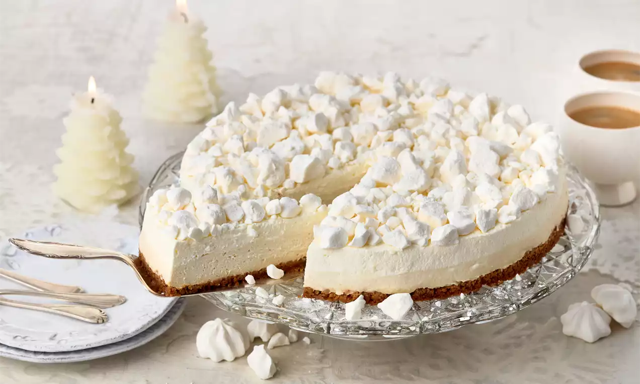 Schneeflöckchen-Torte mit weißer cremiger Füllung auf braunem Boden, bedeckt mit luftigen Baiserstücken auf einer Glasplatte angerichtet