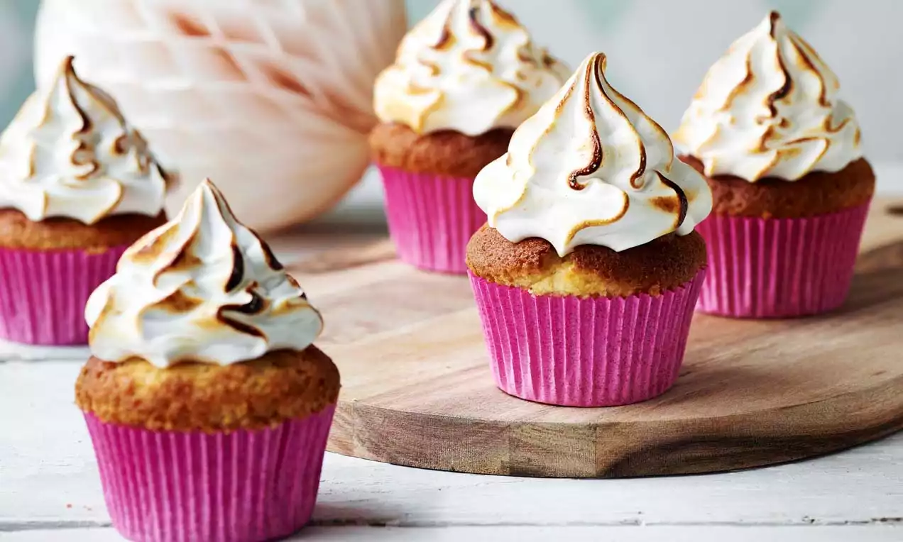 Korkeiksi kuplivat vaahtokarkkihuurteet paahtopinnan sävyttämät, kullankeltaiset muffinipohjat pinkeissä paperivuoissa puisella alustalla