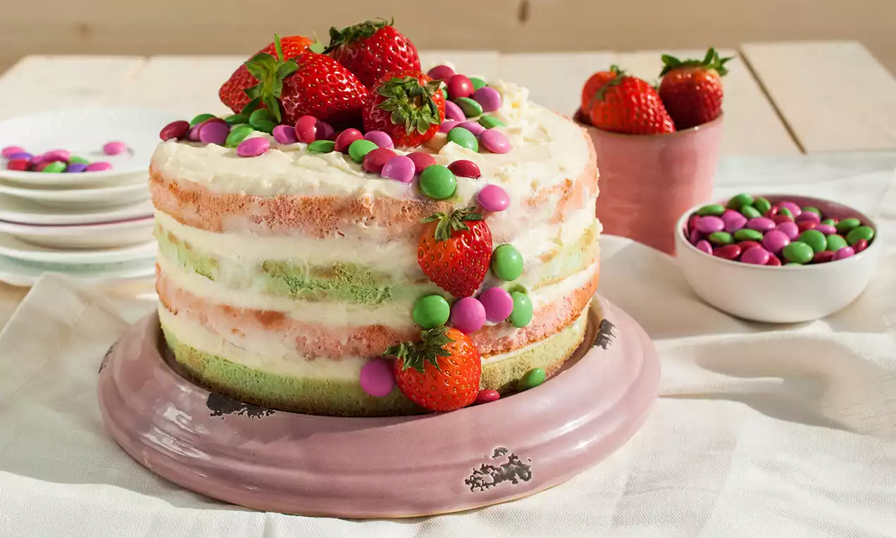 Vrstvená torta s jemným krémom, pastelovými korpusmi, ozdobená čerstvými jahodami a farebnými lentilkami na ružovom podnose 