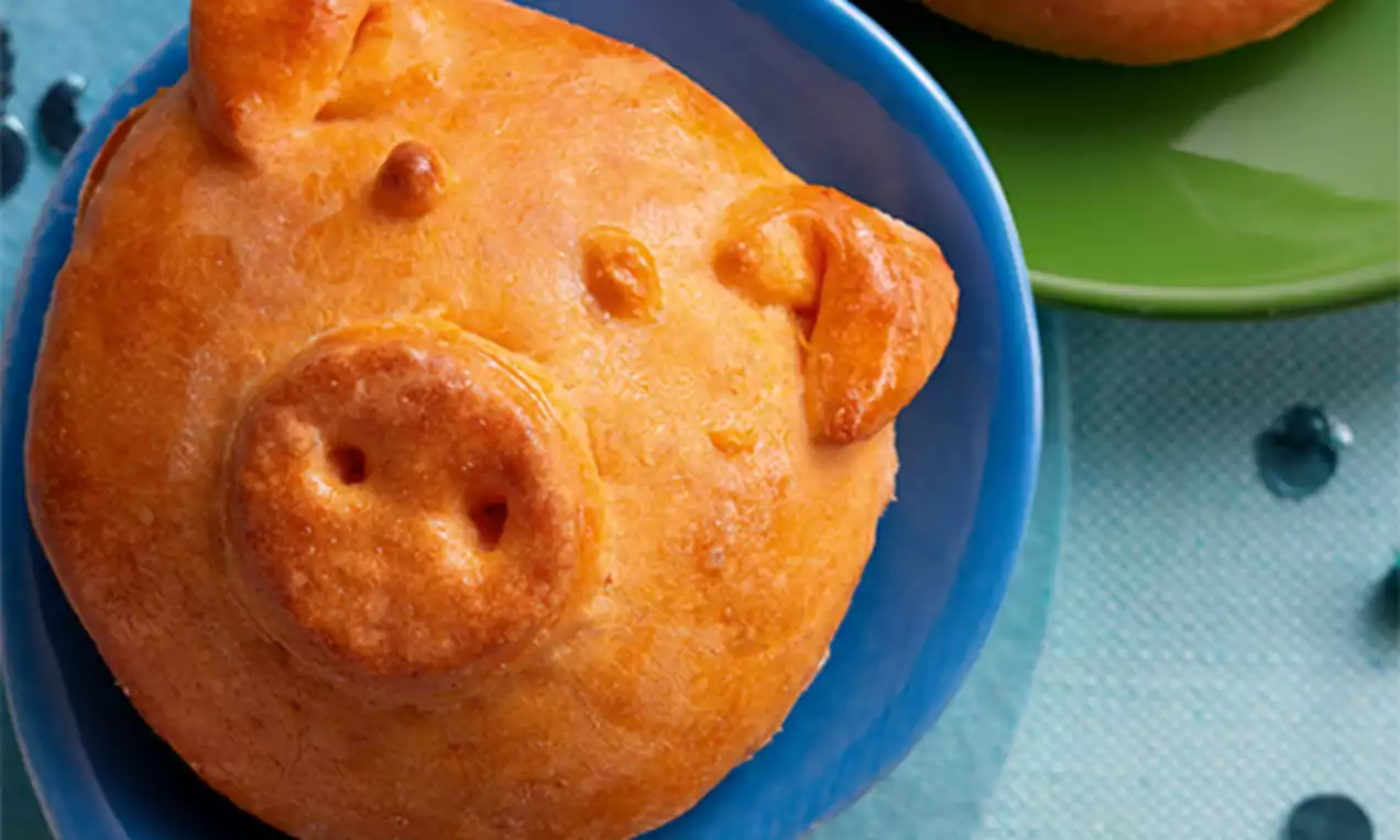 Goudbruin gebakken broodvarkentjes met afgeronde vormen op een blauw bord, omlijst door een groene schaal en glanzende decoratieve kralen