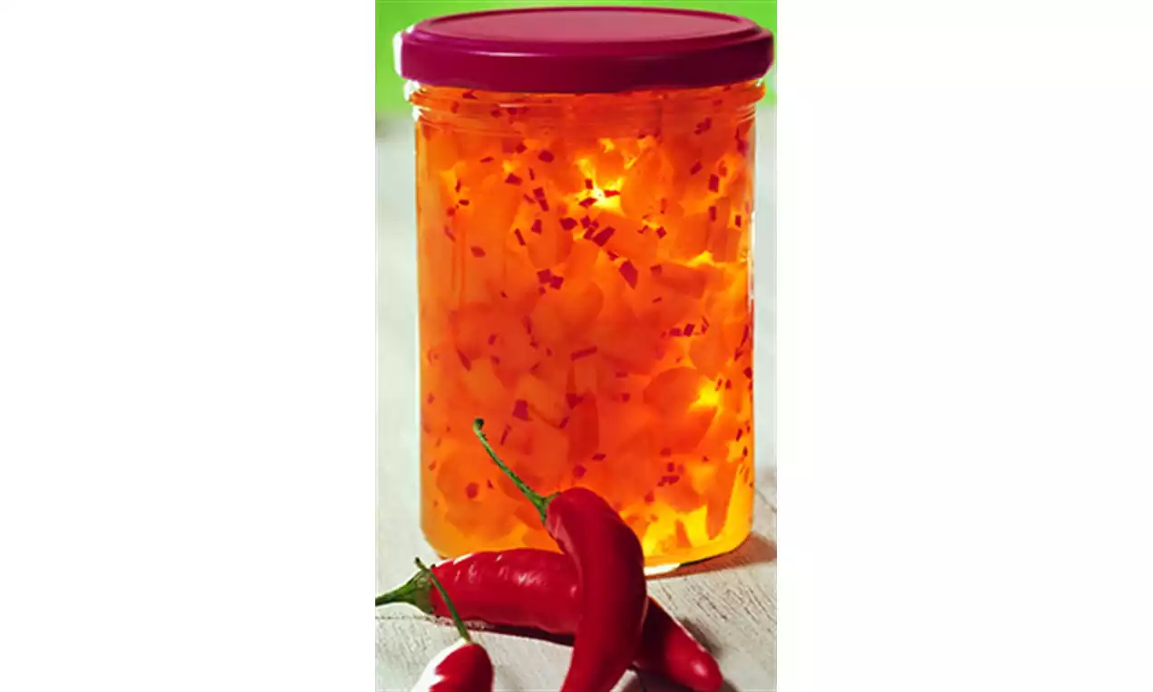 Confiture d'abricots translucide couleur orange vif parsemée de morceaux de piment rouge dans un bocal en verre avec un couvercle pourpre