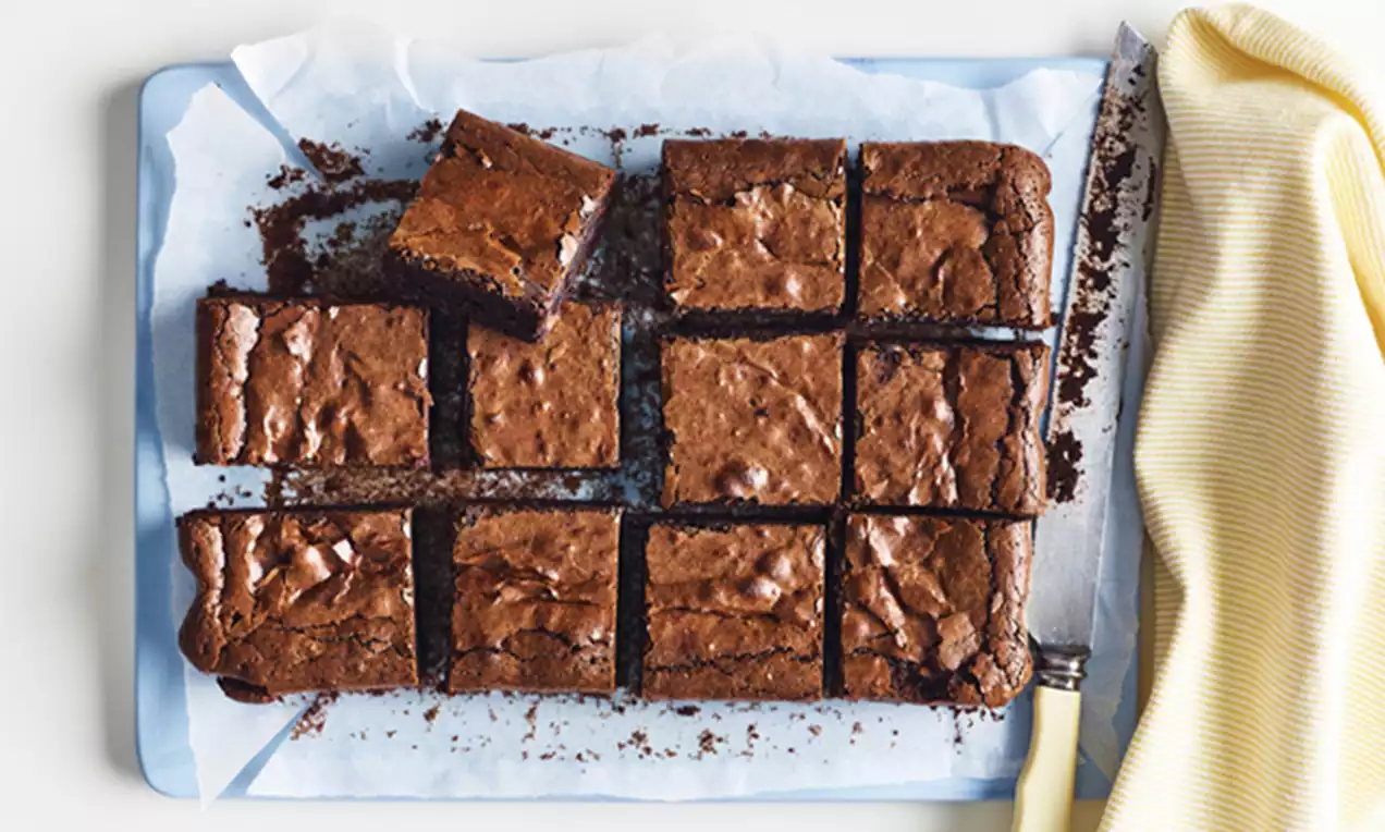 Classic chocolate brownies sliced into neat rectangles with a glossy, crinkled surface resting on white baking paper alongside a knife