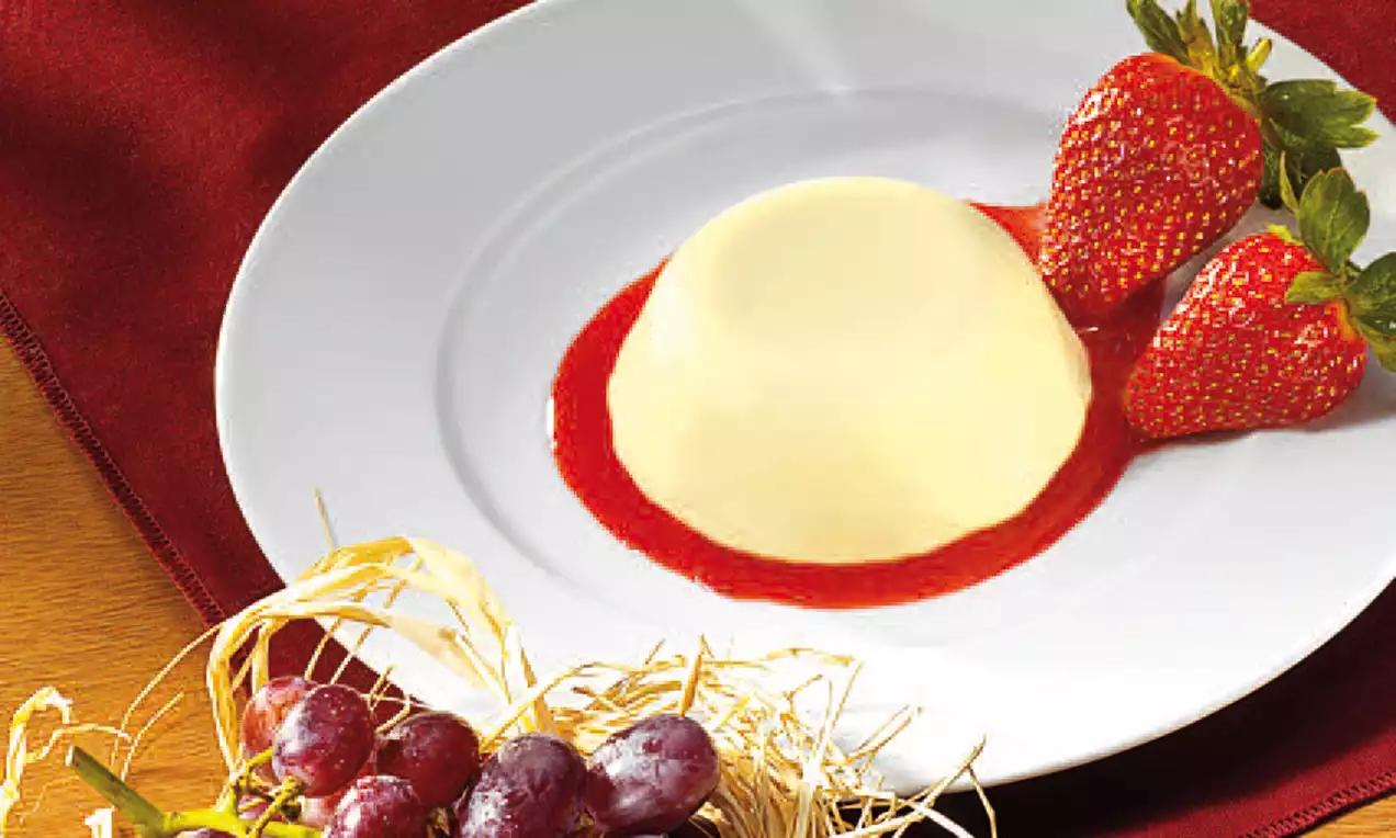 Panna cotta lisse et ivoire posée sur un coulis rouge de fraises, accompagnée de fraises fraîches sur une assiette blanche