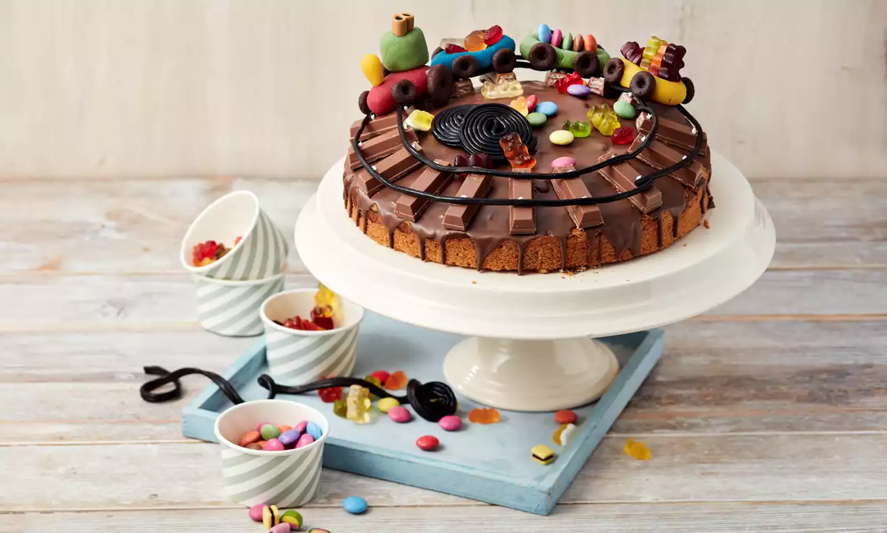 Marmorkuchen mit glänzender Schokoladenglasur, dekoriert mit buntem Süßigkeiten-Eisenbahn-Motiv auf weißer Tortenplatte