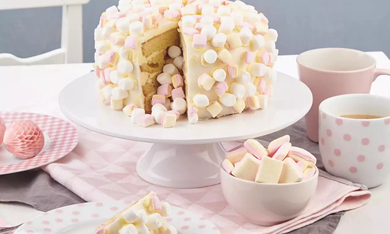 Heller Marshmallow-Kuchen mit weicher gelber Füllung, umhüllt von weißen und rosa Schaumzuckerwürfeln auf weißer Tortenplatte drapiert