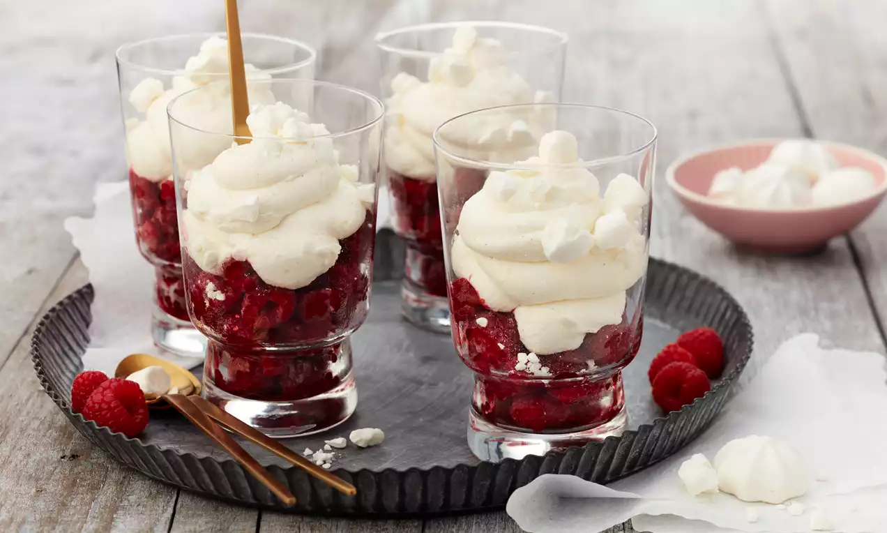 Schneegestöber im Glas mit fluffiger weißer Creme, schichtweise tiefroten Himbeeren und zarten, hellen Baiserbröseln garniert