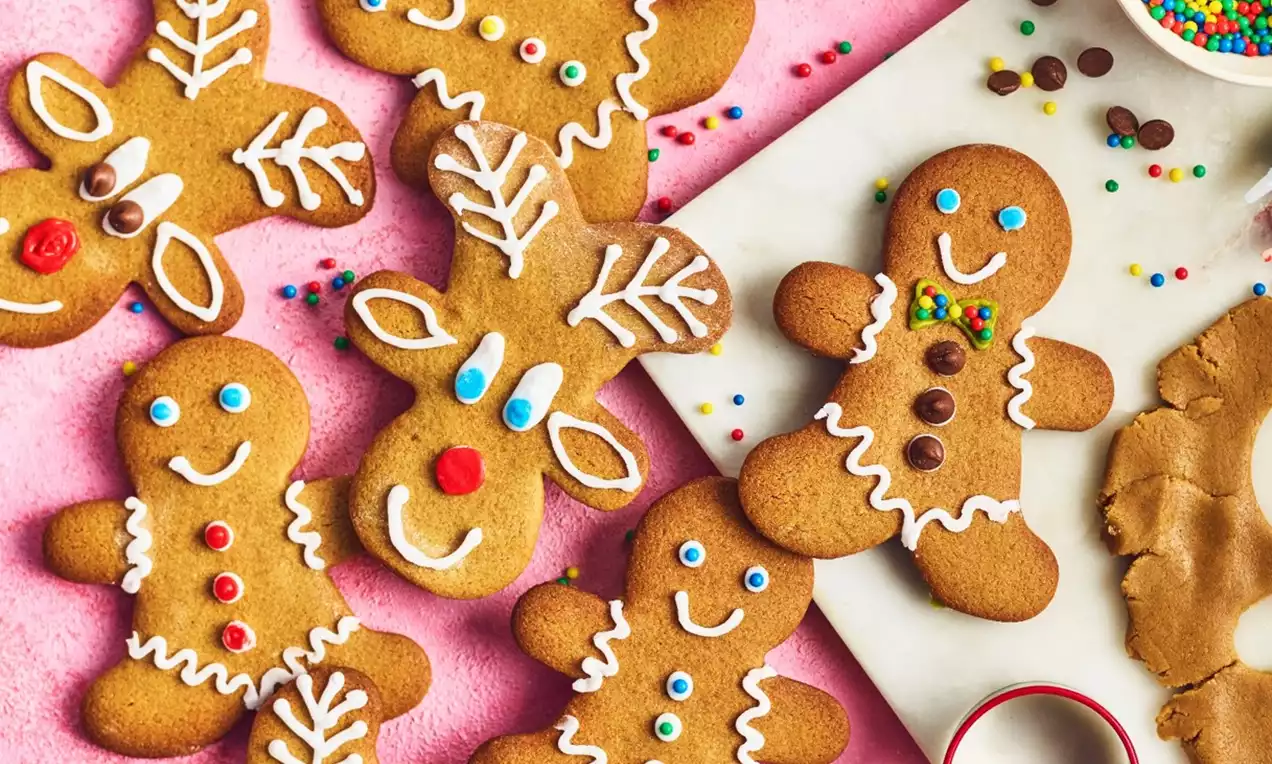 Golden brown gingerbread cookies shaped like reindeer and people, decorated with colorful icing and candy on a pink surface with sprinkles