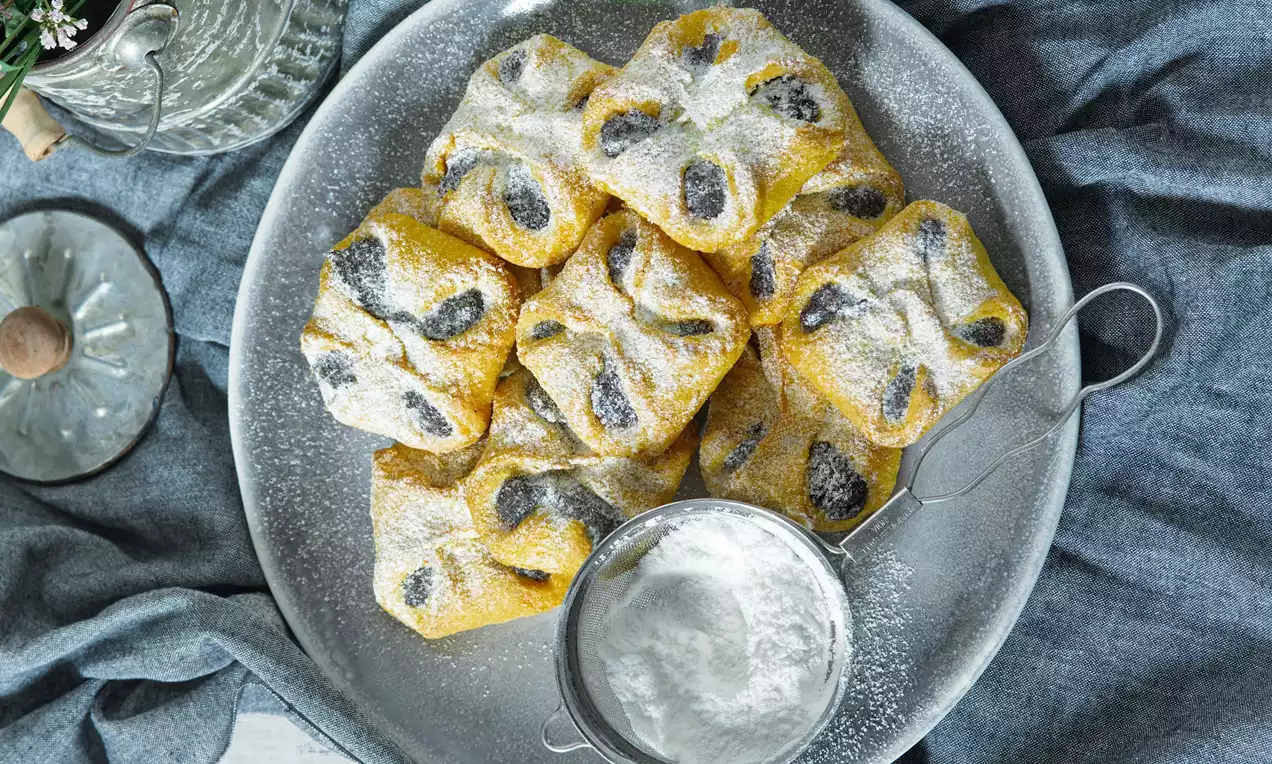 Mrkvovníky vo svetložltom odtieni s posýpkou práškového cukru, štvorcový tvar, tmavé vrstvy plnky, uložené na šedom tanieri