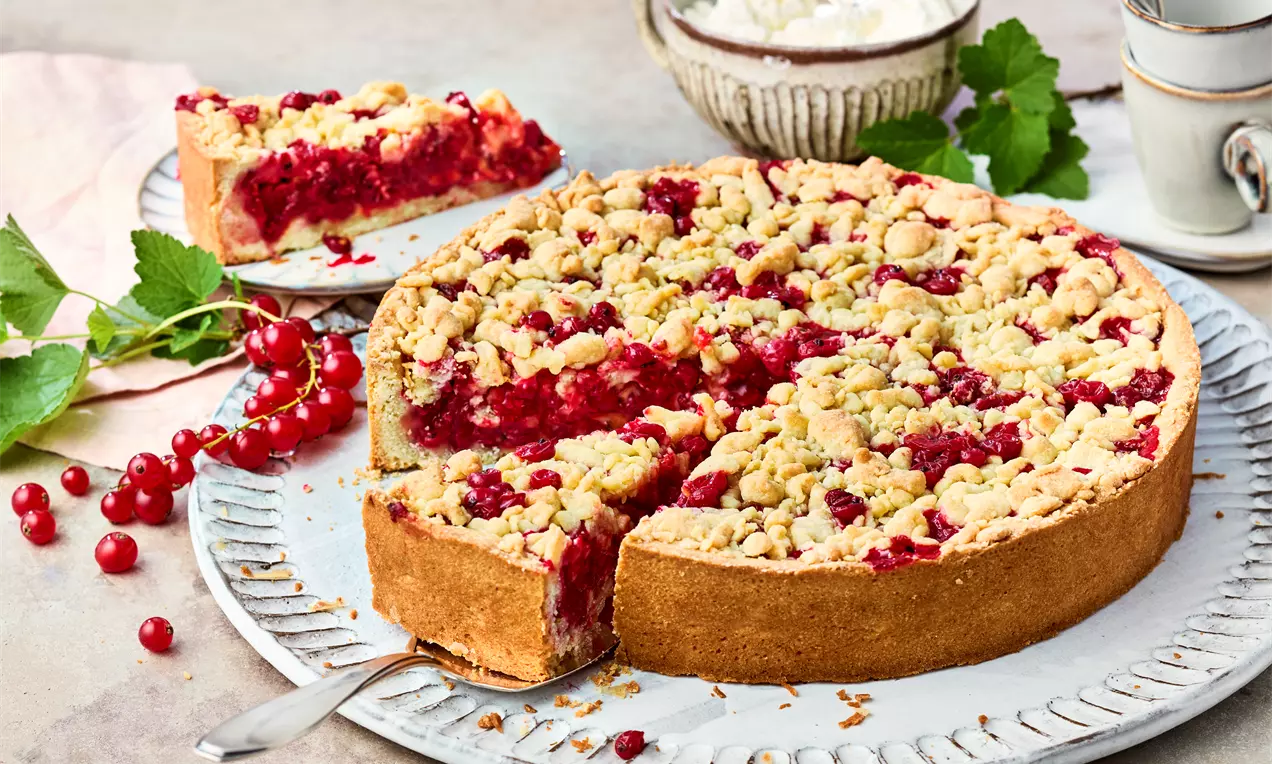 Johannisbeer-Streuselkuchen mit goldbraunem Mürbeteig und knusprigen Streuseln, gefüllt mit leuchtend roten Beeren auf einem weißen Teller
