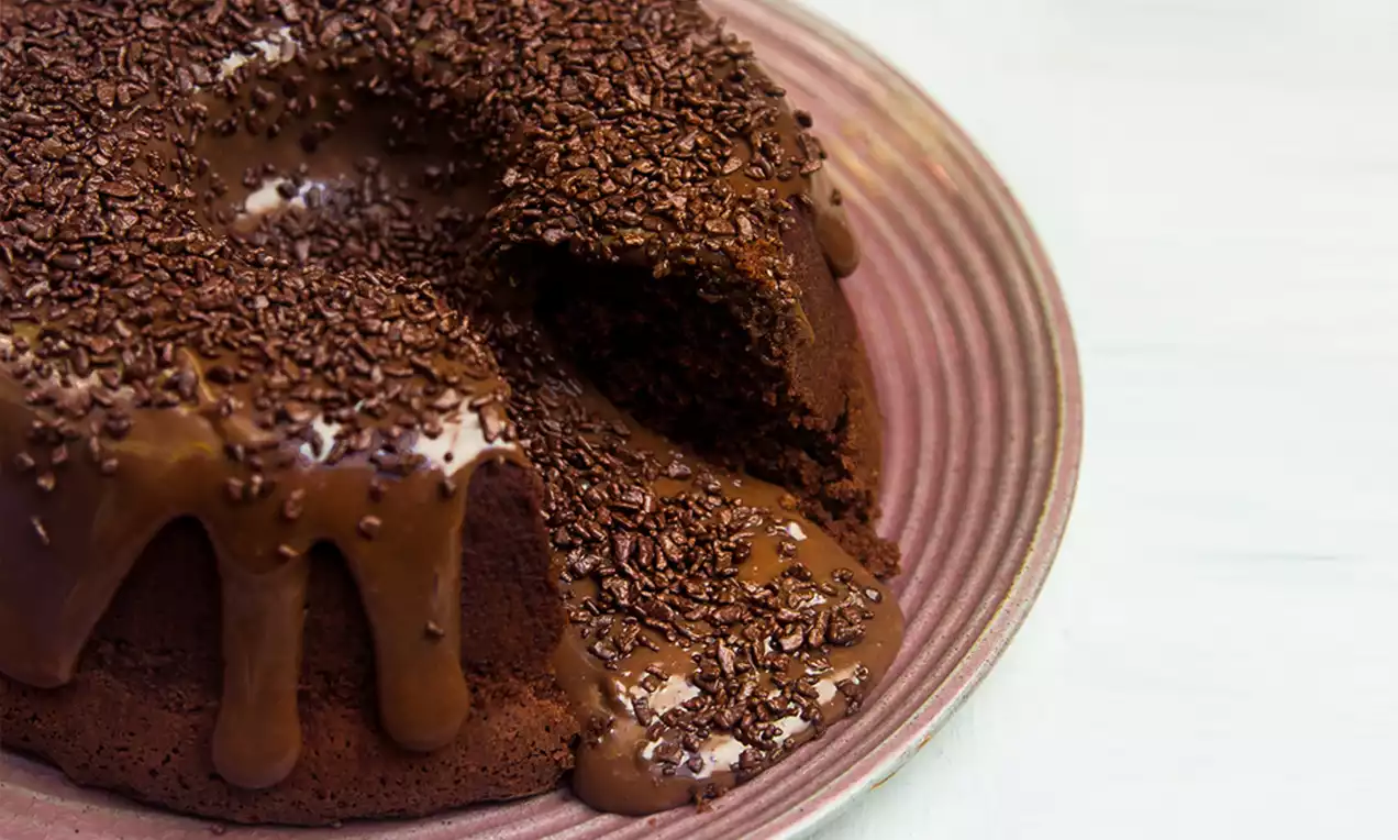 Bolo Vulcão de Chocolate com cobertura de ganache brilhante escorrendo pelo topo, fatia mostrando miolo úmido e raspas de chocolate