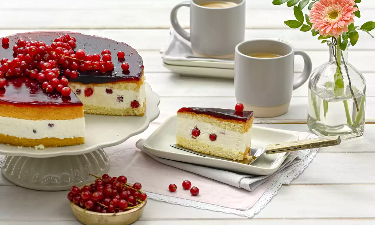 Johannisbeer-Torte mit rotem Gelee, weißer Cremefüllung und goldbraunem Boden, dekoriert mit frischen Beeren auf einer weißen Tortenplatte