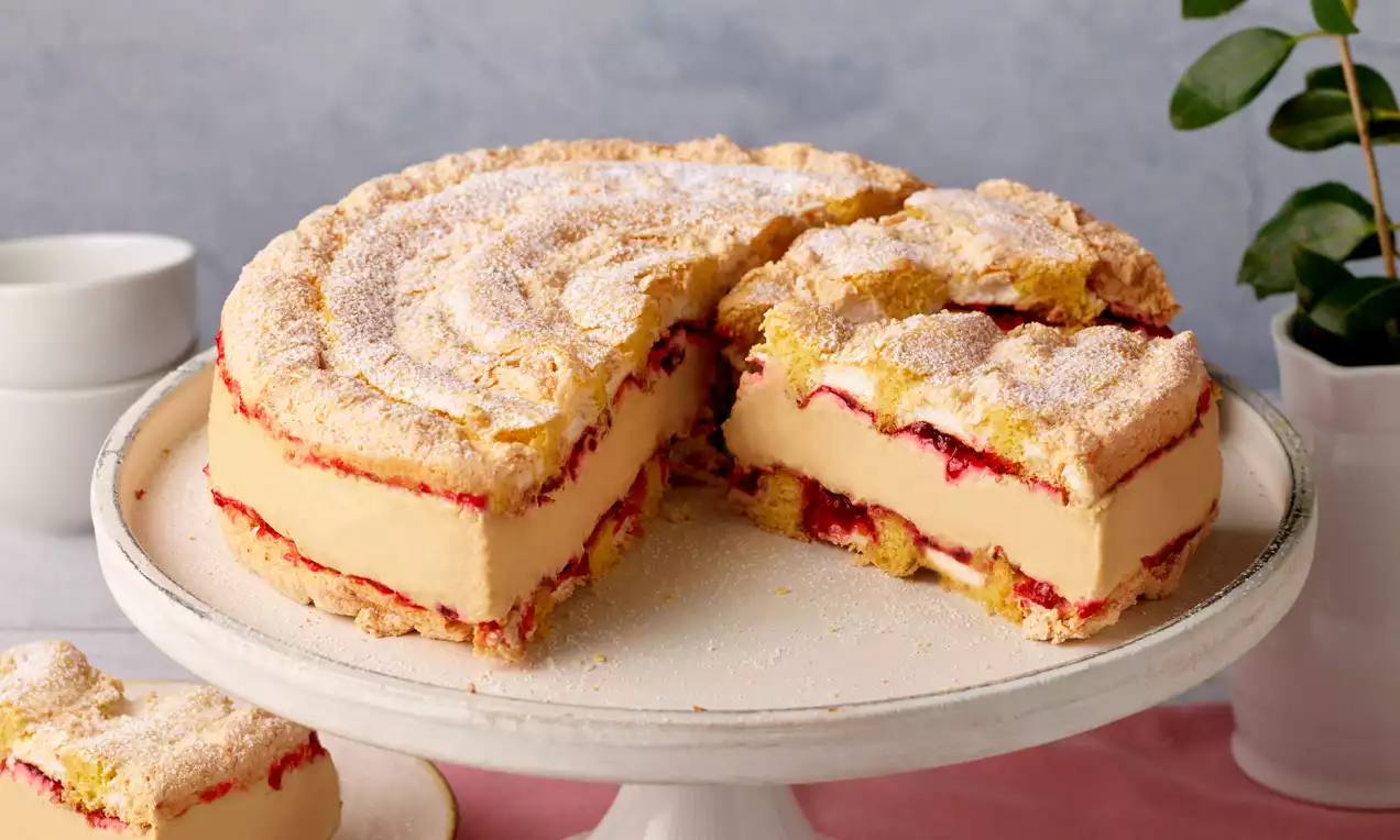 Kardinaltorte mit goldgelber Creme, luftigem Biskuit, roten Marmeladenschichten und Puderzucker auf weißer Tortenplatte angerichtet
