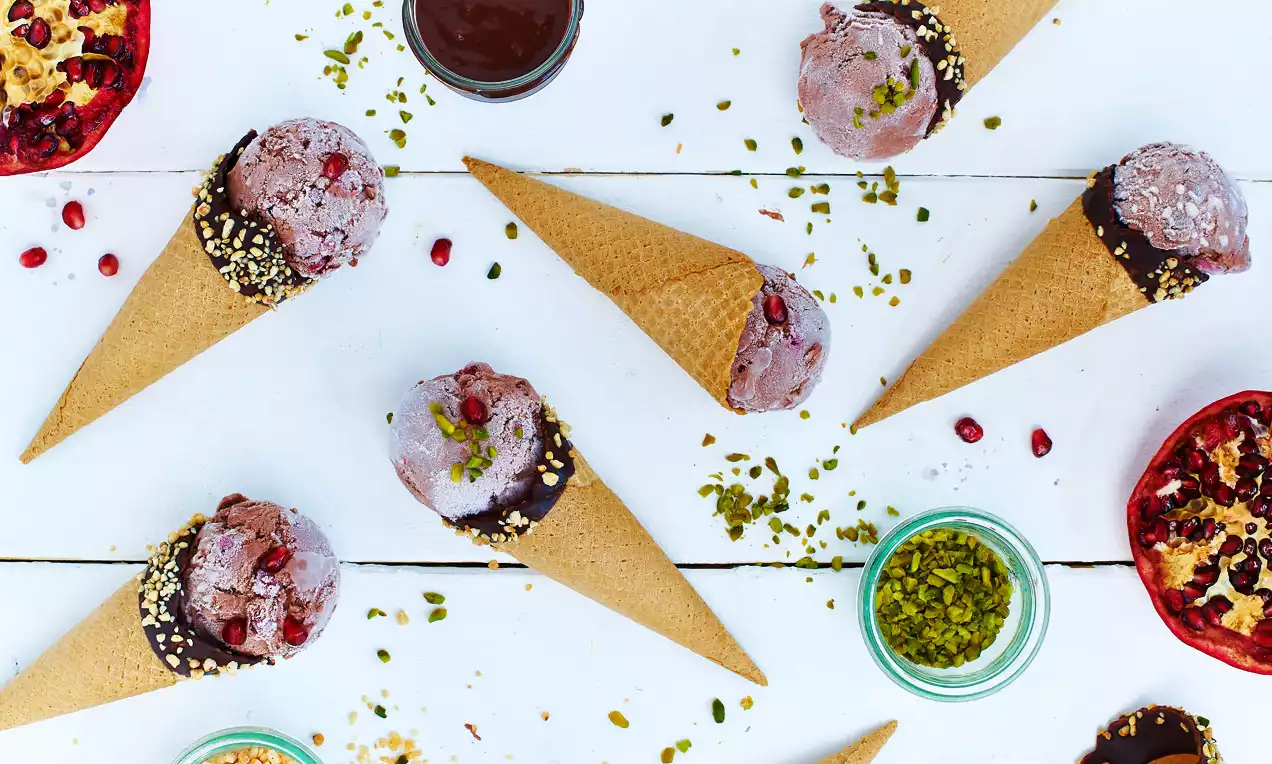 Chocoladeijs in beige hoorntjes, bestrooid met pistachenoten, gegarneerd met granaatappelpitjes, op een witte achtergrond met granaatappels