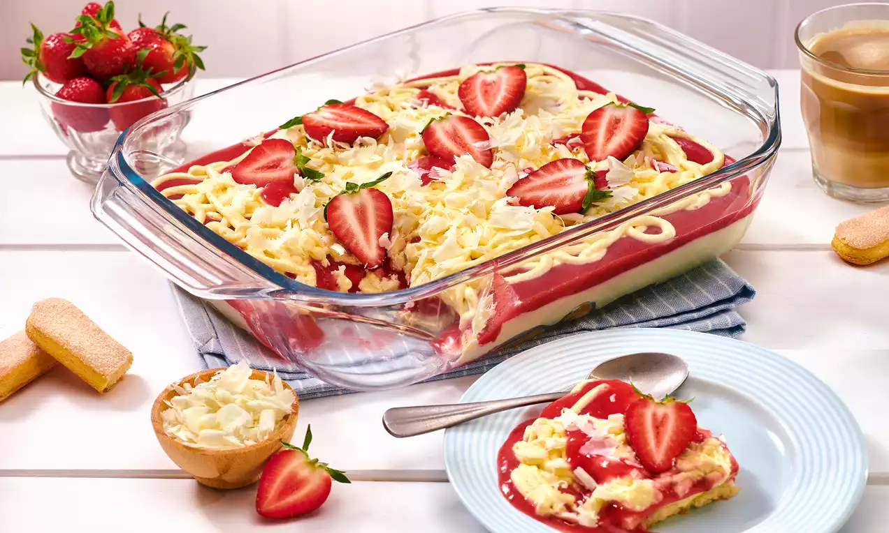 In einer gläsernen Form mit Vanilleschichten, roten Erdbeersauce und weißer Schokoladenraspeln, garniert mit frischen Erdbeeren