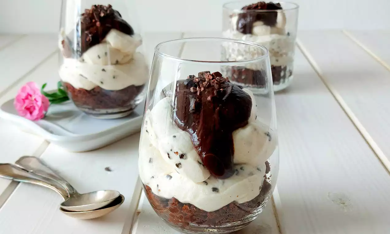 Kakaový základ s krémovou bielou šľahačkou posiatou čokoládovými kúskami, korunovaný lesklou čokoládovou polevou v sklenenom pohári