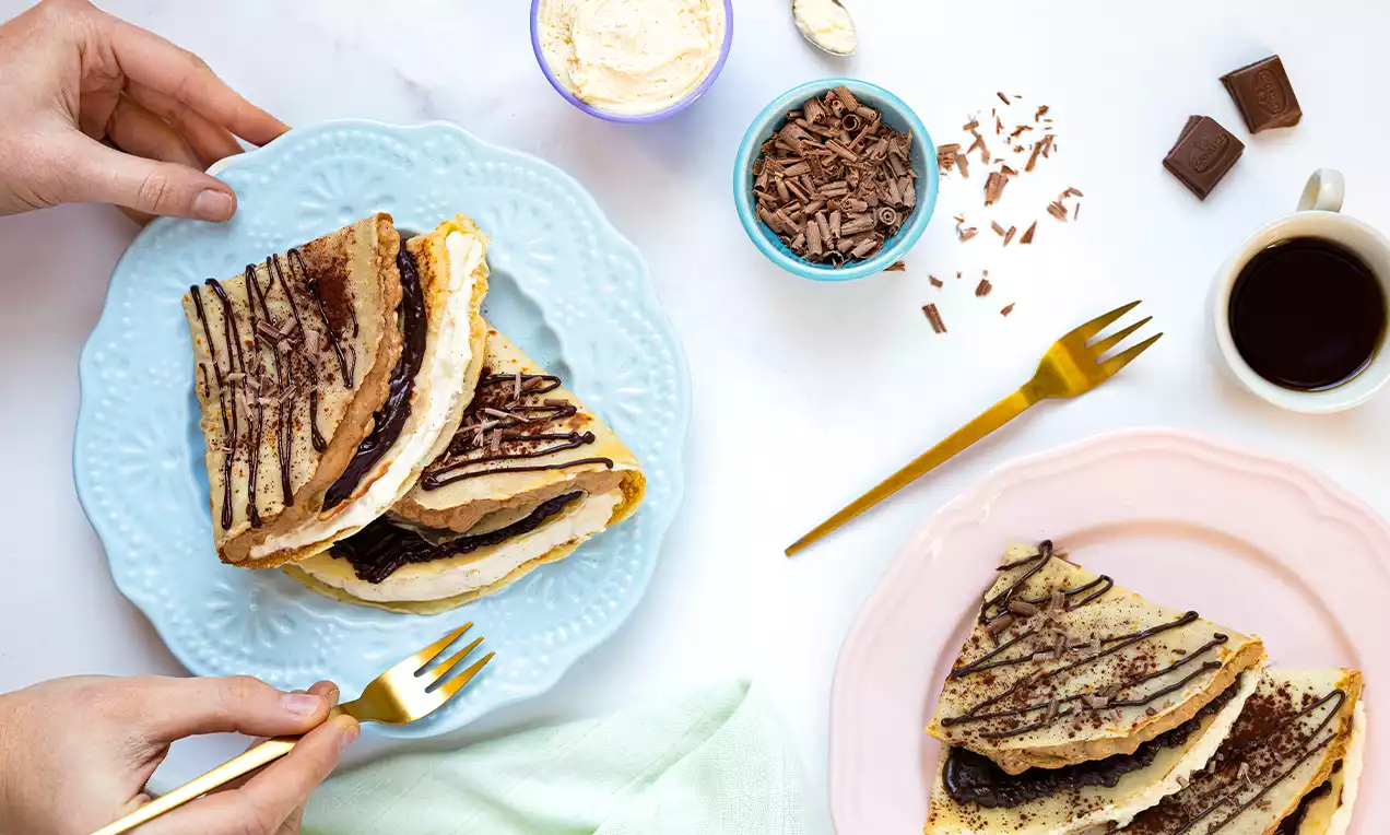 Licht goudbruine Tiramisu-pannenkoeken met romige vulling en chocoladesaus gedrapeerd, geserveerd op pastelblauwe en roze borden
