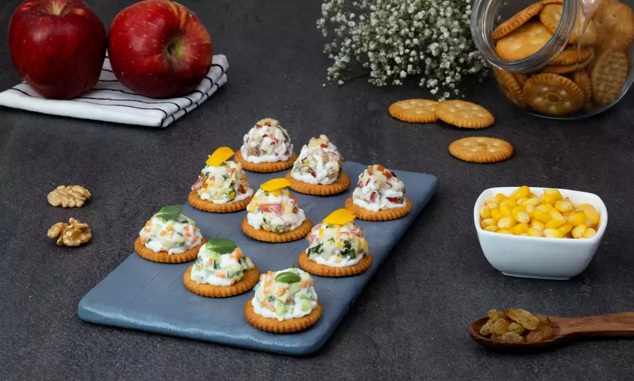 Round golden crackers topped with colourful creamy vegetable fillings, garnished with herbs and served on a grey slate platter