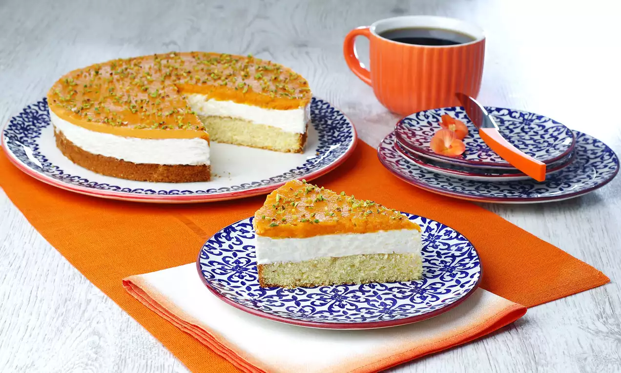 Bal kabaklı lorlu pasta, beyaz ve mavi desenli tabakta, katmanlı dokusu ile üstü turuncu ve ince yeşil fıstık parçaları serpilmiş