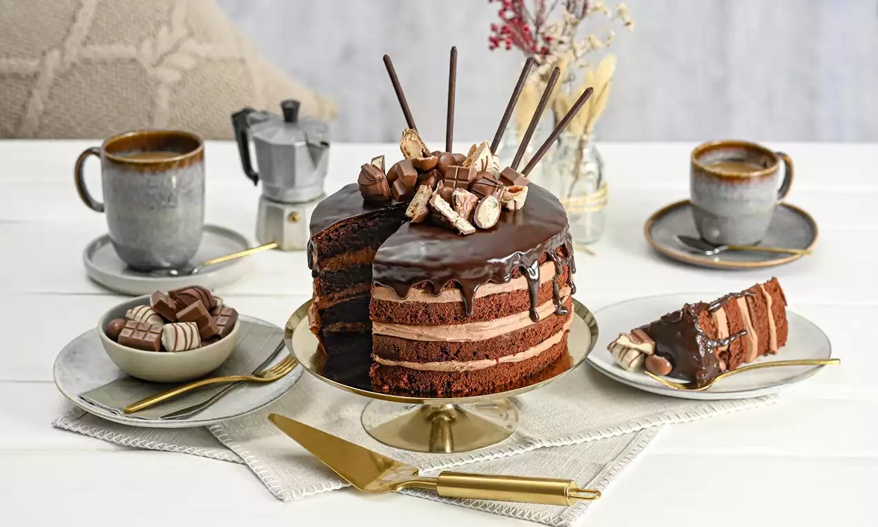 Layered chocolate cake with glossy dark ganache, stacked with chocolate cream, topped with striped chocolates on a gold cake stand