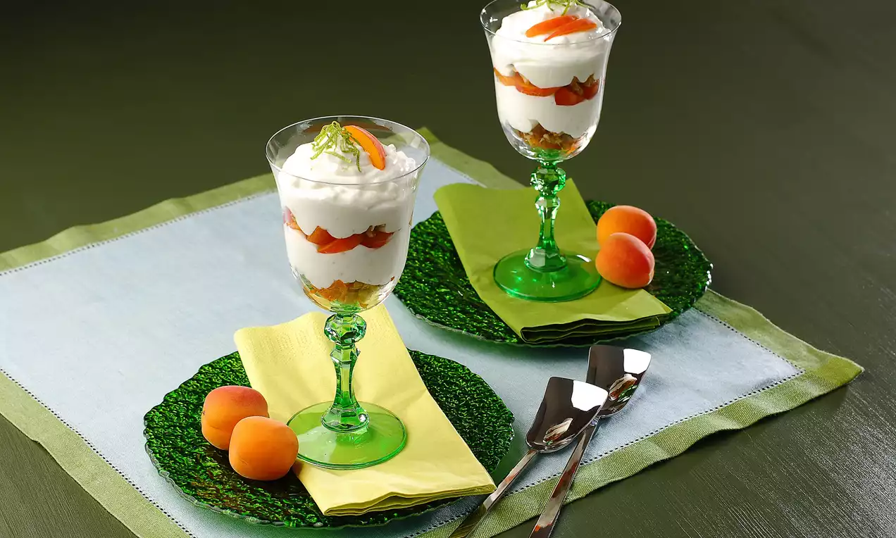 Yeşil cam kupalarda sunulan kayısılı sütlaç, kat kat kremsi doku ve taze kayısılarla süslü, yeşil tabakta zarif biçimde yerleştirilmiş