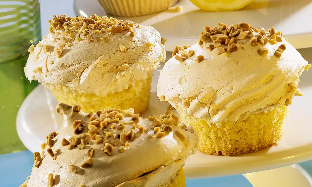 Morbidi tortini dorati con una copertura di meringa cremosa color avorio, guarniti con granella di nocciole su un piatto bianco