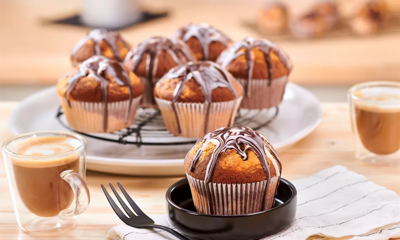 Marmor-Muffins mit hellen und dunklen Teigwirbeln, goldbraunen Oberseiten in Papierförmchen auf einem weißen Teller angerichtet