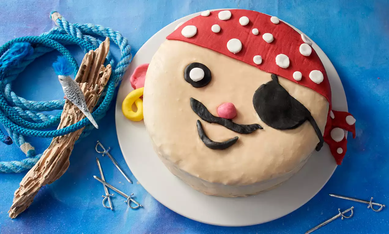 Runde Torte auf weißem Teller, dekoriert mit rotem Fondant, weißen Punkten, gelbem und schwarzem Marzipan sowie maritimer Verzierung