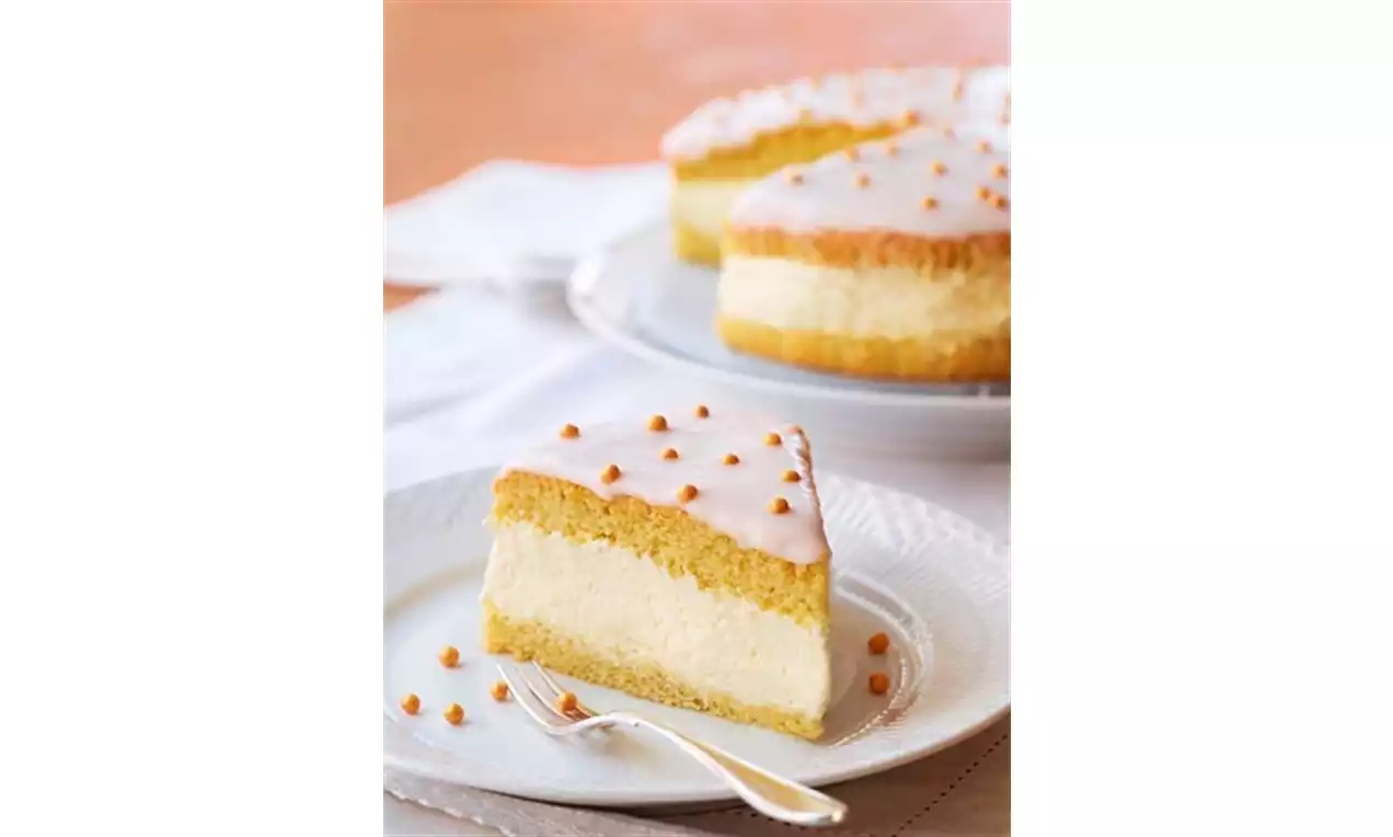 Sokerikuorrutettu vaaleankeltainen kerroskakku, täyteläinen kerma keskellä, koristeena ruskeita palloja valkoisella keraamisella lautasella