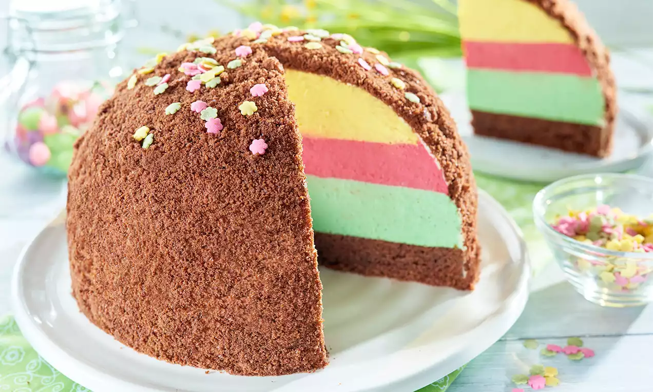 Guľovitá torta s čokoládovými strúhankovými drobkami, vrstvami žltej, ružovej a zelenej krémovej náplne, ozdobená farebnými kvietkami
