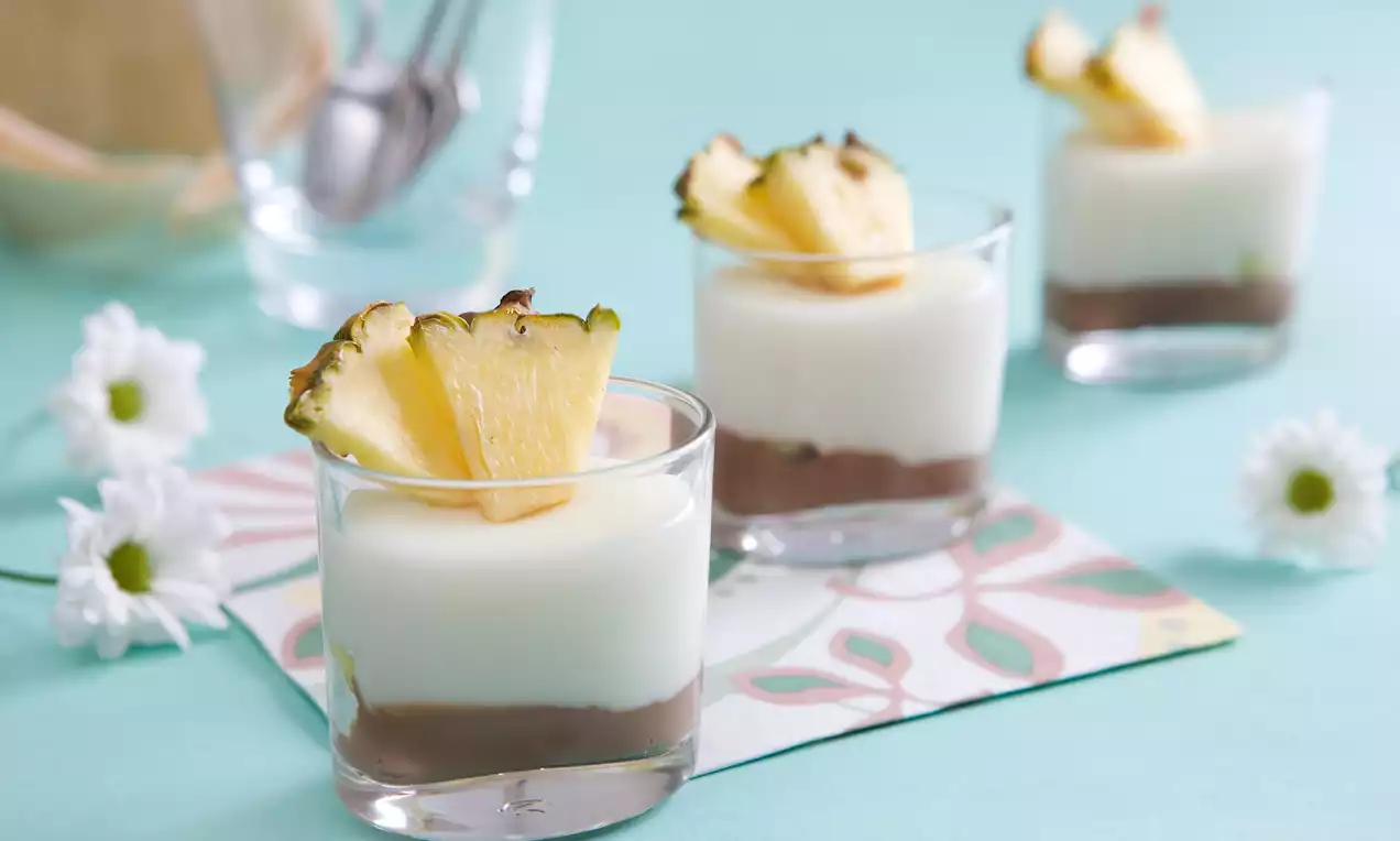 Krémovo biely puding na čokoládovom základe v sklených pohároch, ozdobený šťavnatým kúskom ananásu, položený na pastelovej servítke