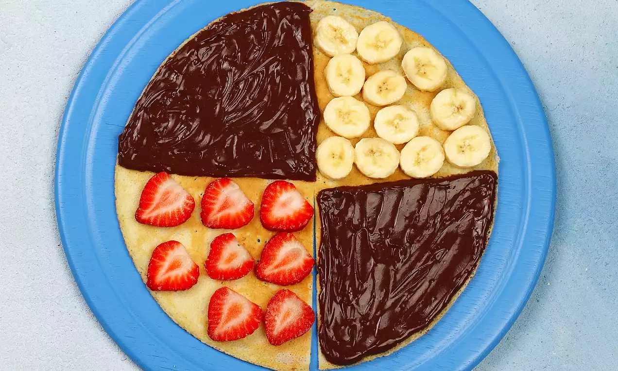 Düz mavi tabakta ince krep, bir kısmı çilek dilimleri, bir kısmı muz dilimleri, diğer kısımları çikolata kreması ile kaplanmış