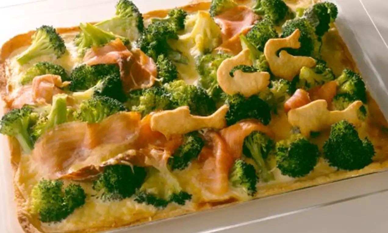 Rechteckige Quiche mit goldgelbem Boden, grünen Brokkoliröschen, zarten Lachsscheiben und kleinen goldbraunen Teigmaßfiguren