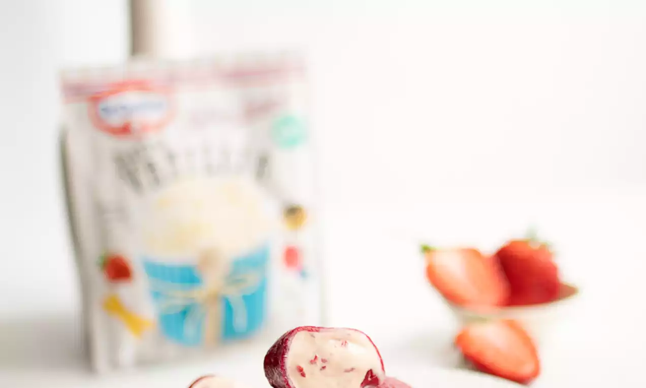 Sladoled Mochi jarko crvene boje s glatkom sjajnom koricom i kremastim punjenjem, naslagan na bijelom tanjuru uz dio svježe jagode