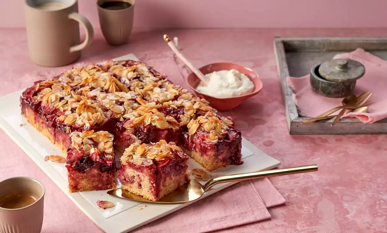 Laktosefreier Kuchen mit roten Kirschen im hellen Rührteig, knusprigem goldbraunem Mandel-Topping und leichtem Puderzucker