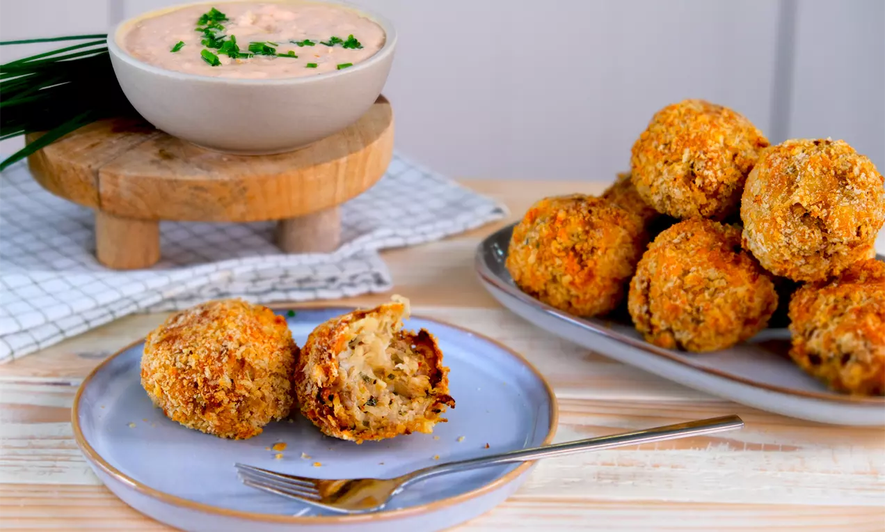 Knusprige Sauerkraut‑Balls aus dem Airfryer auf Teller und Platte; eine Kugel aufgebrochen und zeigt die saftige Füllung. Dazu ein Dip in einer Schale auf Holzpodest und frische Kräuter.