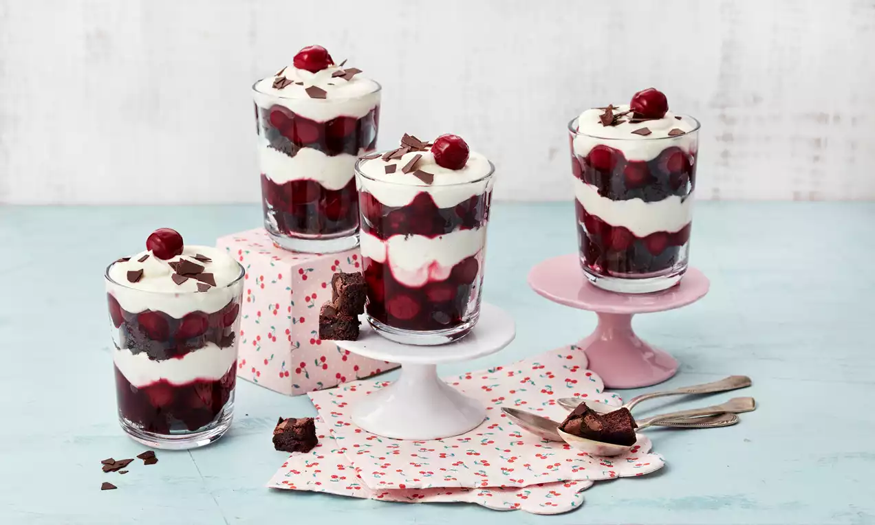 Schwarzwälder-Kirsch-Dessert im Glas mit abwechselnden Schichten aus weißer Sahnecreme und dunkler Kirschfüllung, dekoriert mit Schokoraspeln und Kirschen