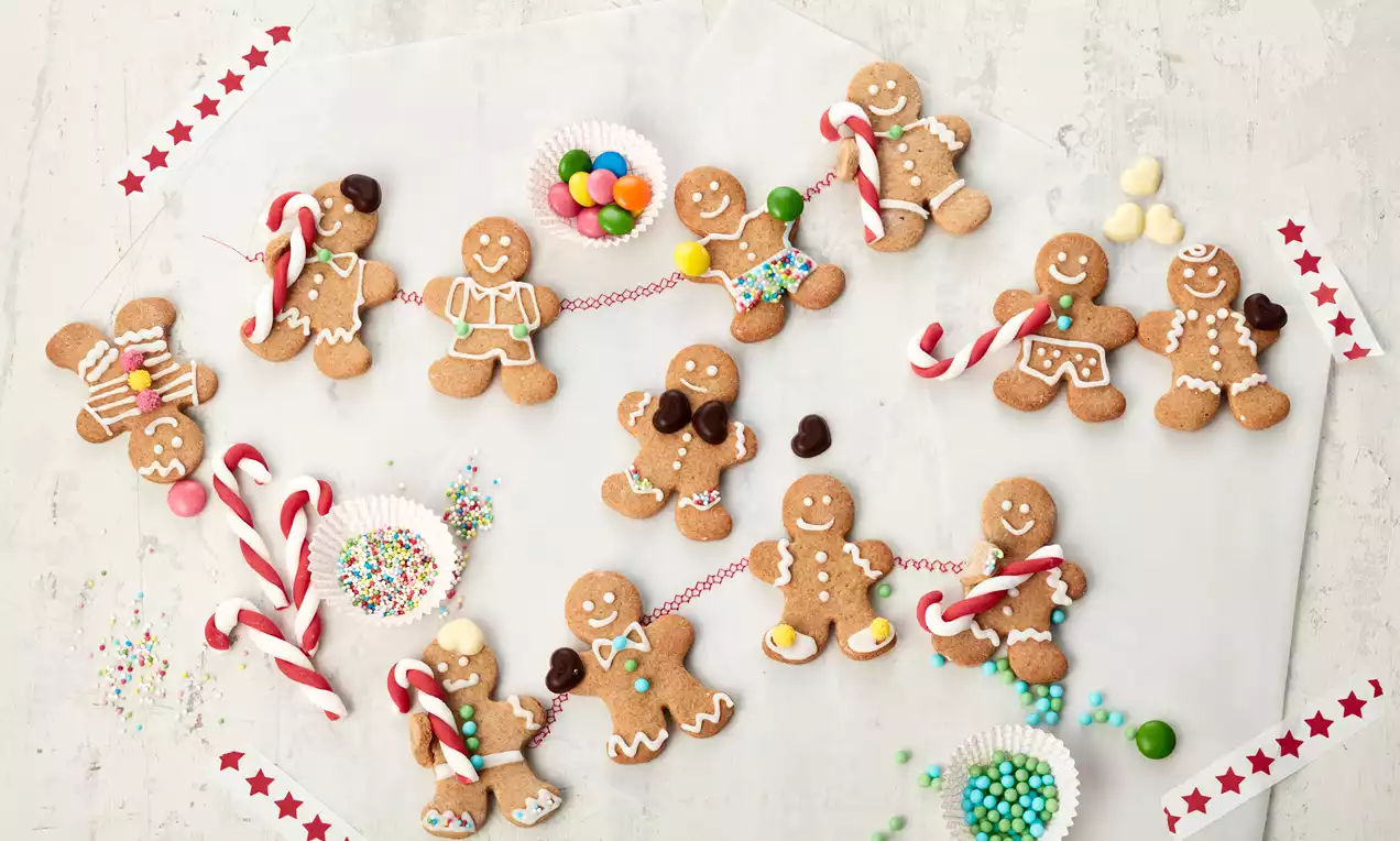 Lebkuchenmänner in warmem Braun, verziert mit buntem Zuckerguss und bunten Details, umgeben von Zuckerstangen und kleinen Süßigkeiten